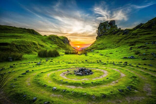 Vibrant spiral of green grasses in mountain range, with pile of rocks in middle of spiral